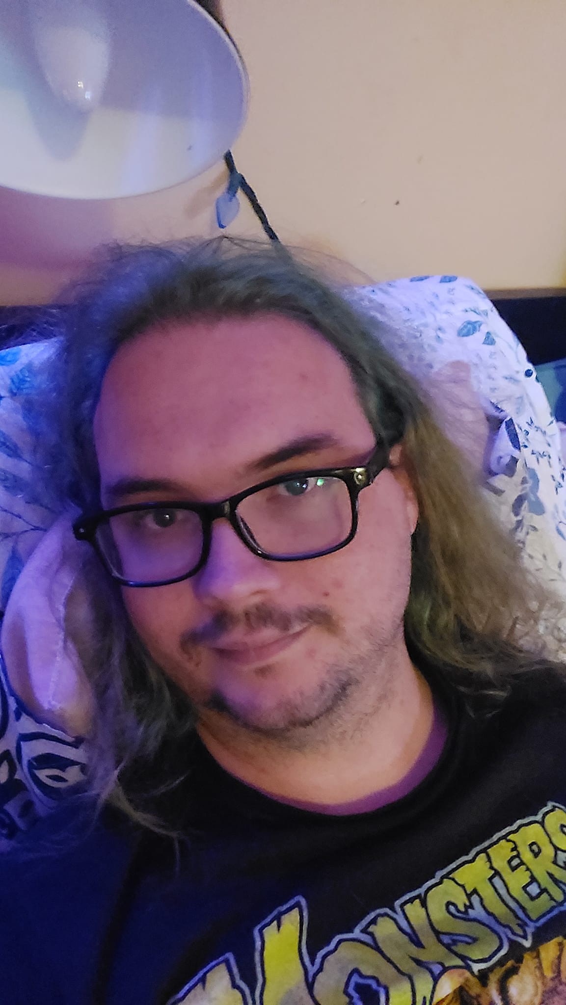 A man with long green hair and no beard lies in bed watching 50s horror movies